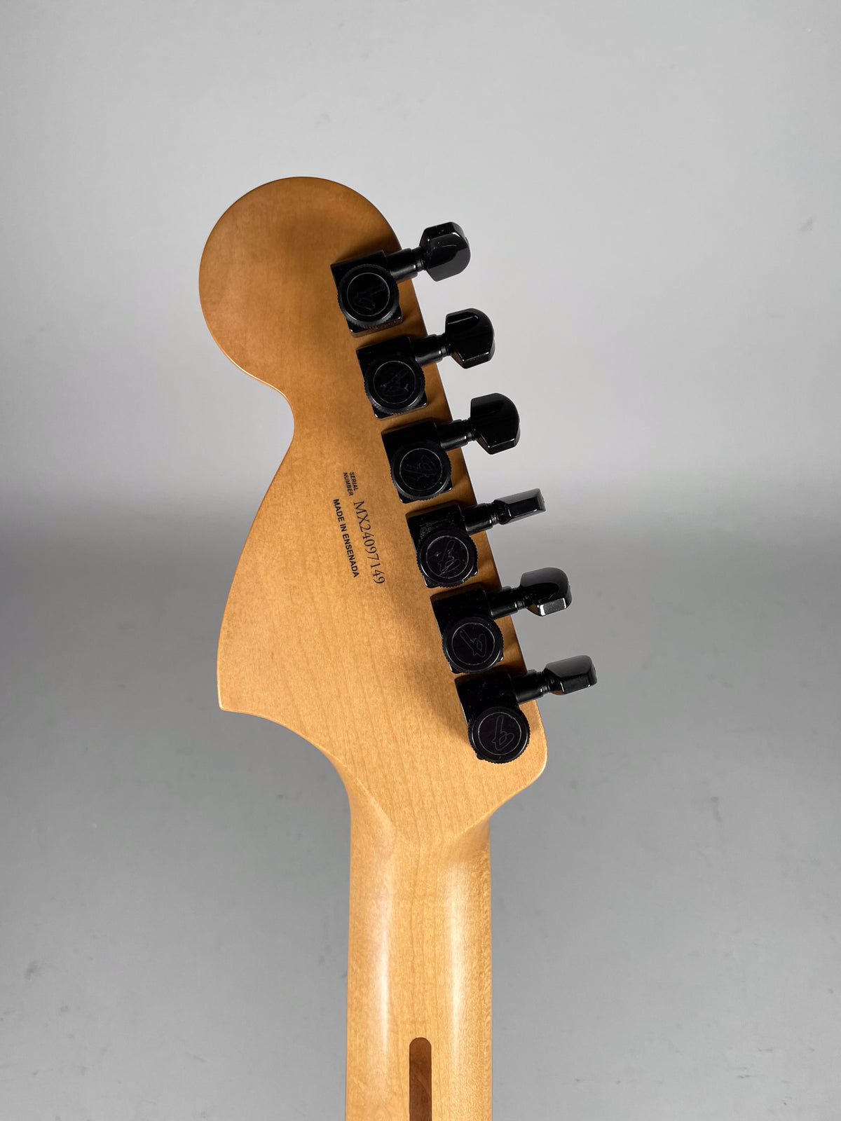 The back of a light wood guitar headstock and neck, with six black tuning pegs.