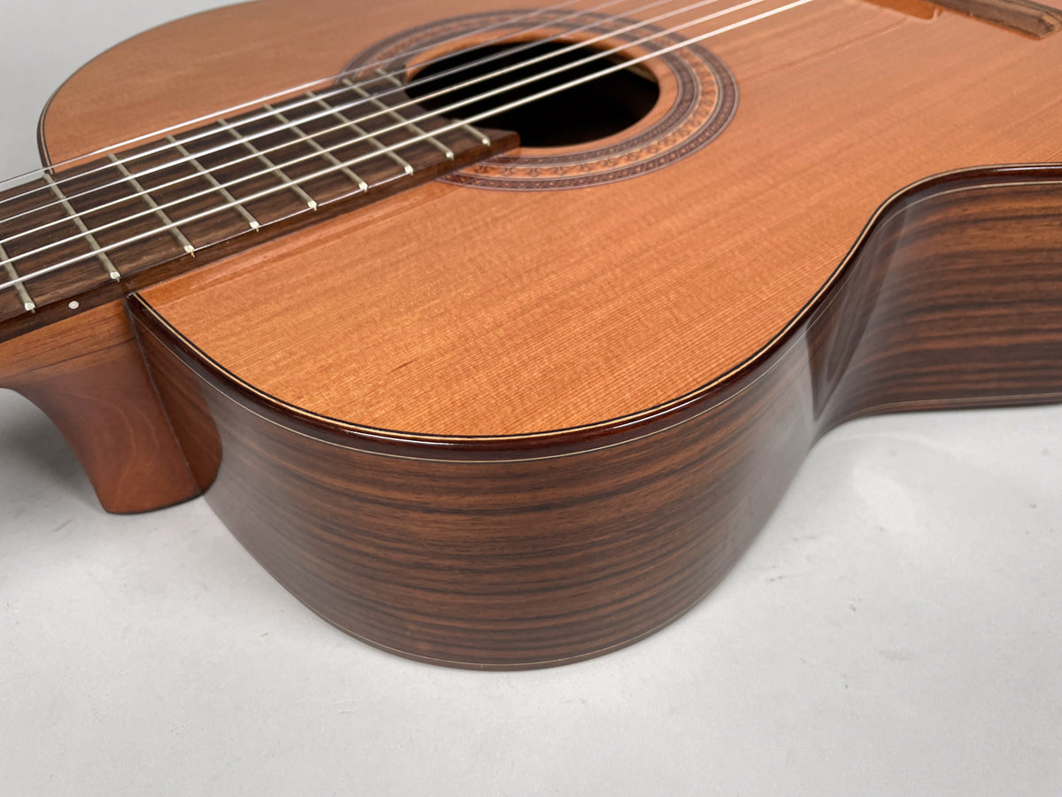 Close-up of a classical guitar, showing the light brown top, dark striped sides, soundhole rosette, and fretboard with nylon strings.