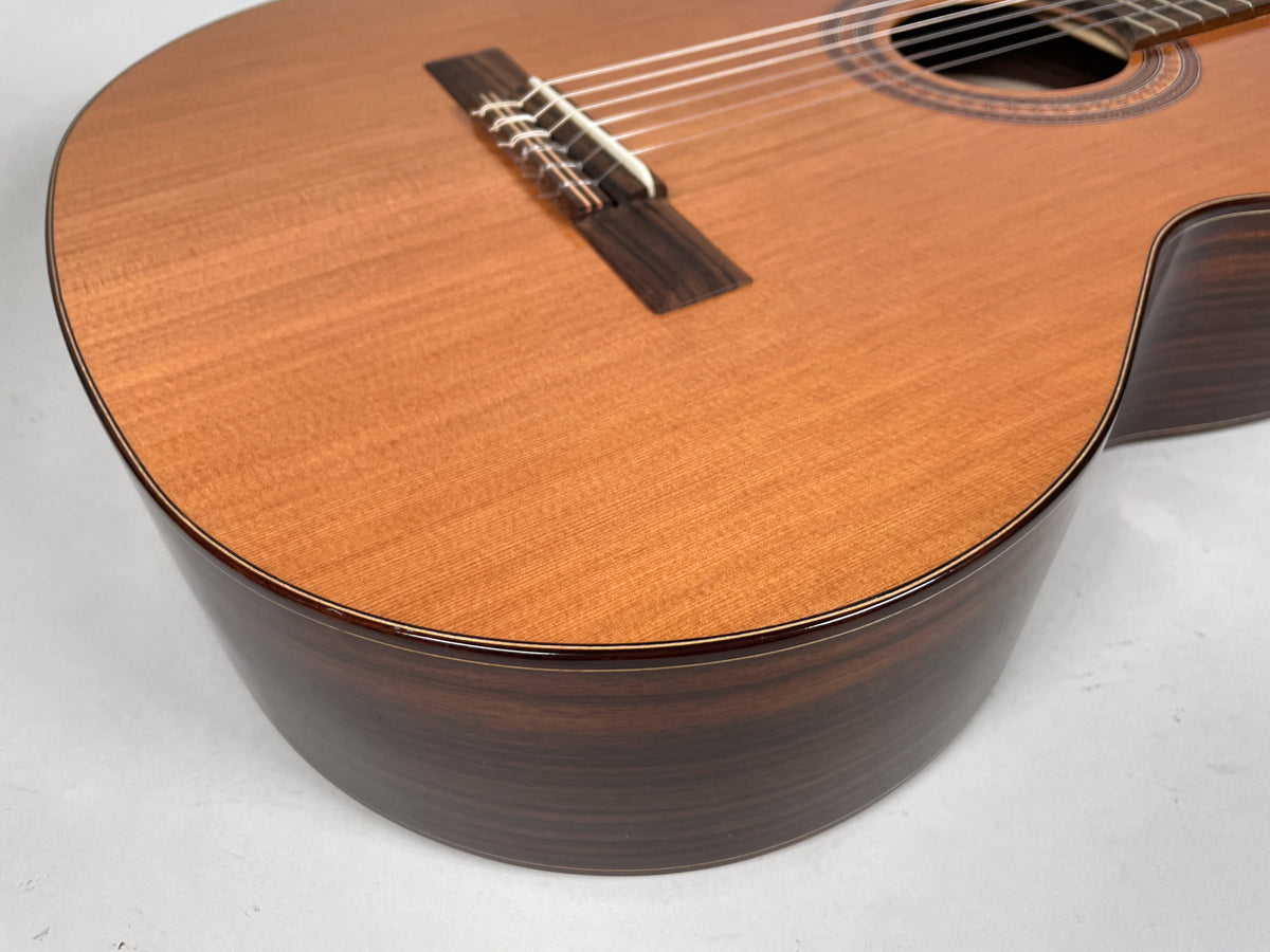 Close-up of the guitar's lower bout, showing the light brown top, dark brown sides, and the bridge with white nylon strings.