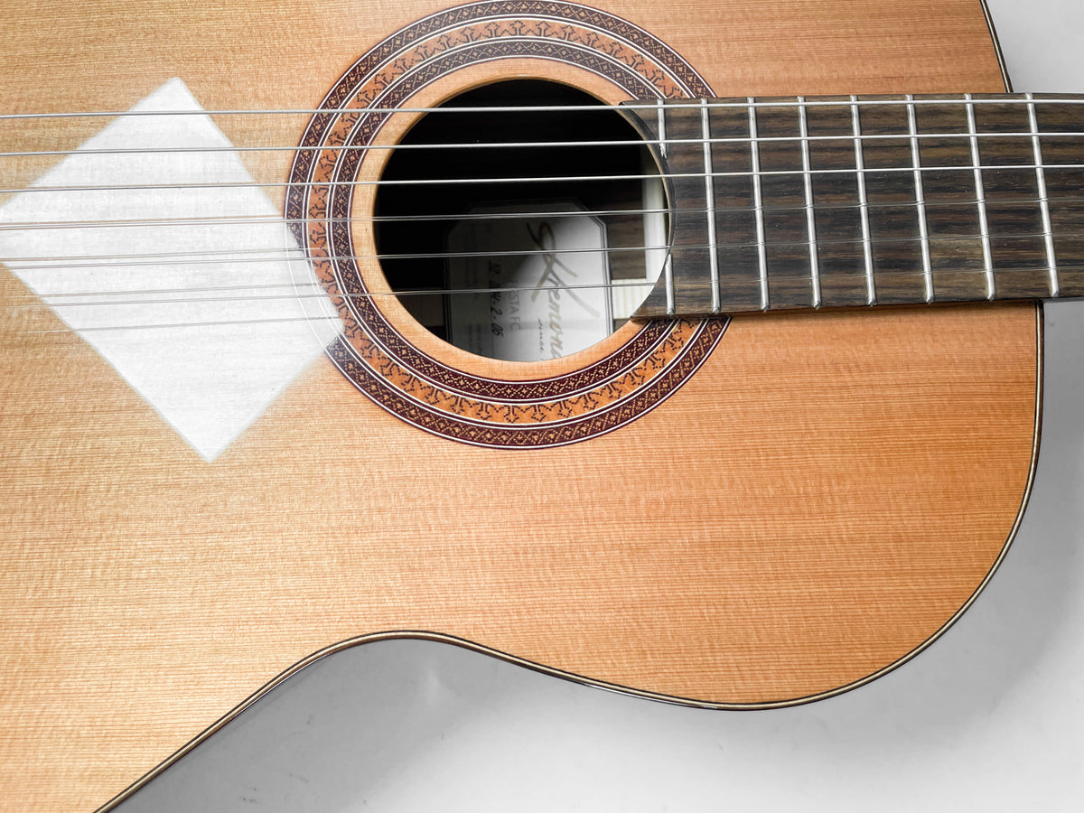 Close-up of the guitar's light wood body, showing the soundhole with a decorative rosette and the dark fretboard extending over the body.