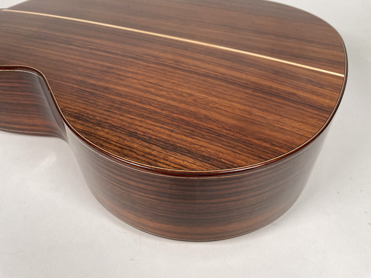 Close-up of the guitar's lower bout and waist, showing the dark brown wood grain, glossy finish, and light-colored binding and backstrip.
