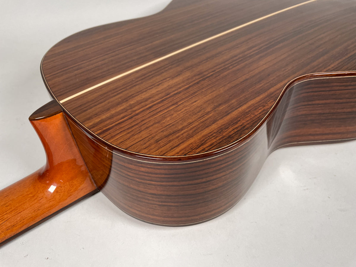 The guitar's dark brown, striped back and sides are visible, with a light wood center stripe and binding, and a glossy amber neck heel.