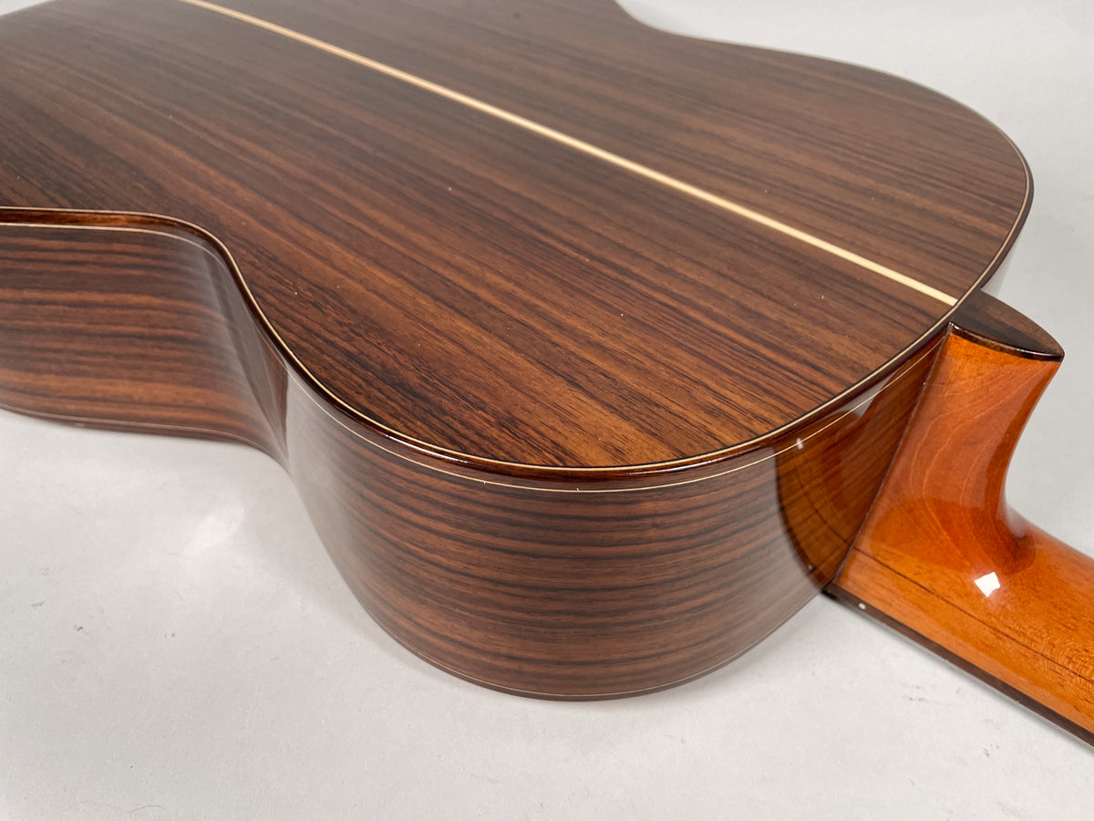 The guitar's dark brown, striped back and sides are visible from the upper bout, with a light wood center strip and a glossy neck heel.