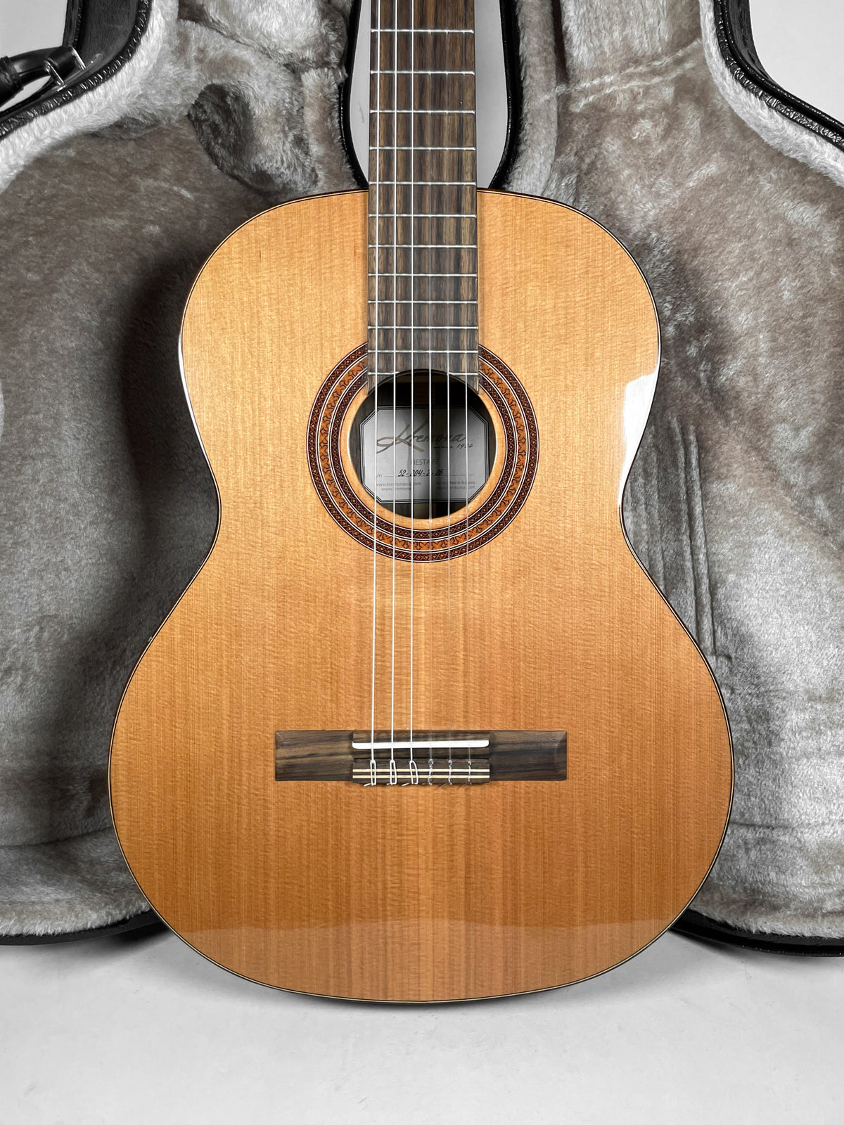 Full front view of the light brown acoustic guitar, showing its glossy finish, dark wood bridge, and intricate rosette around the soundhole.