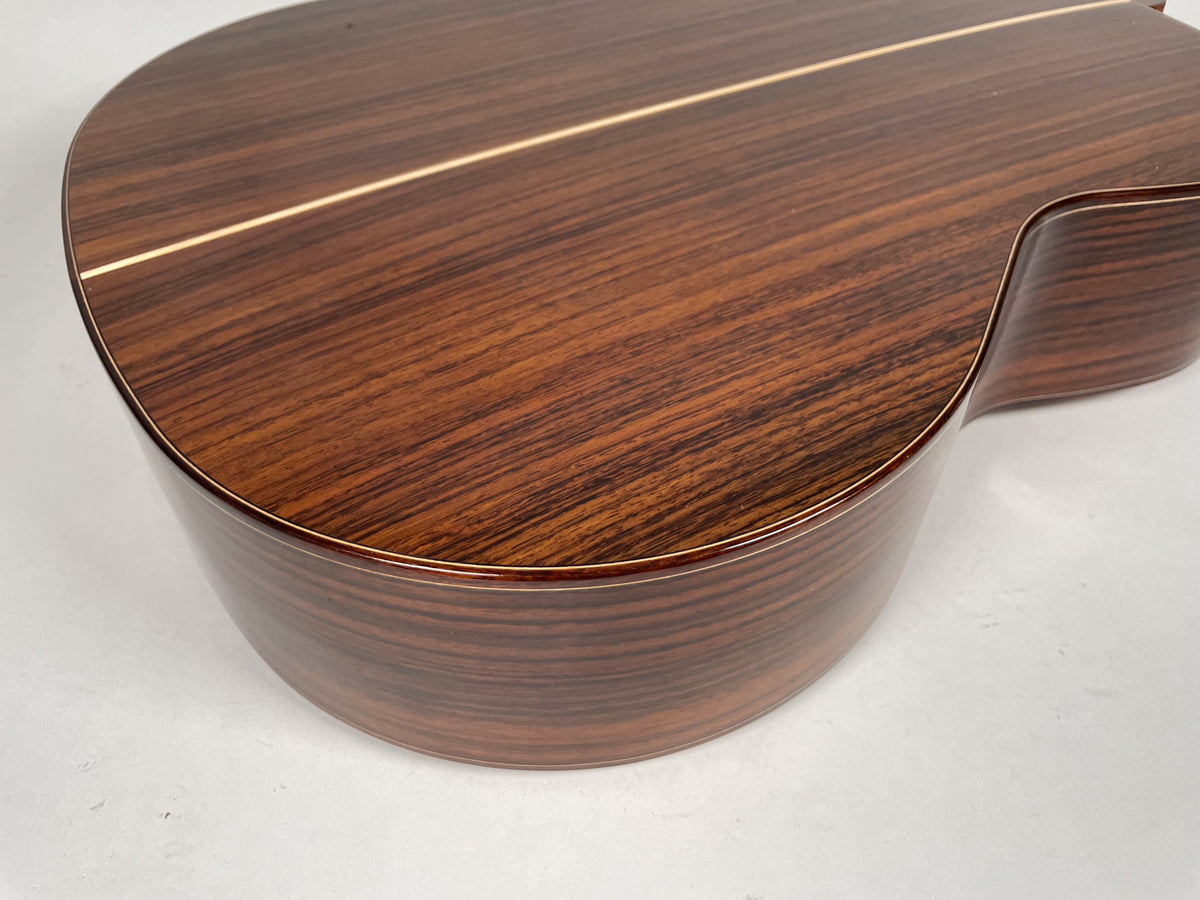The guitar's dark brown, striped wood back and side are angled, revealing a light-colored center strip and thin binding around the edges.
