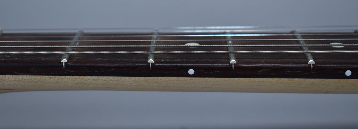 Close-up of the dark fretboard and light maple neck, showing white dot inlays and silver frets and strings.