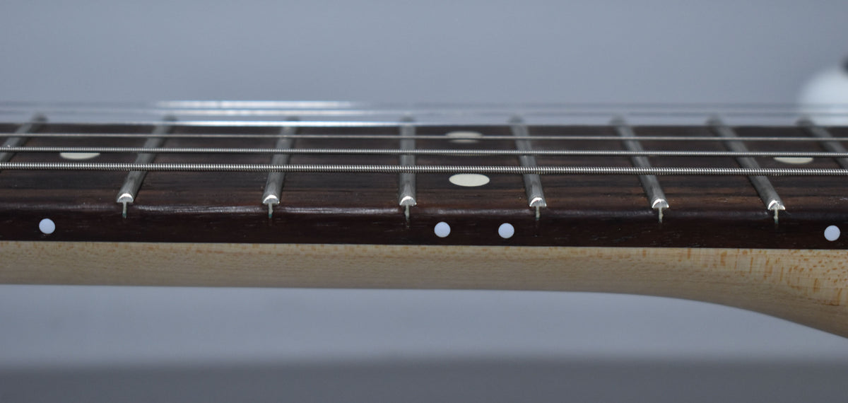 Close-up of the guitar's dark fretboard with white dot inlays and side markers, showing silver frets and strings.