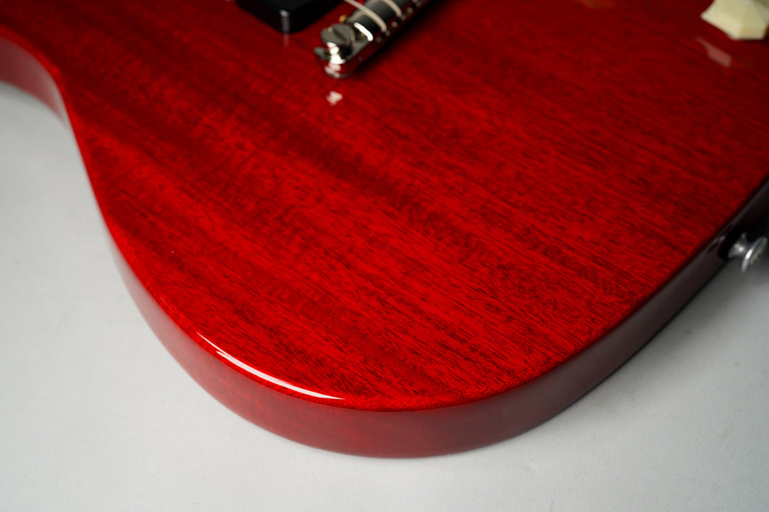 Close-up of the cherry red guitar body, showing the wood grain through the glossy finish, with a chrome bridge visible at the top.
