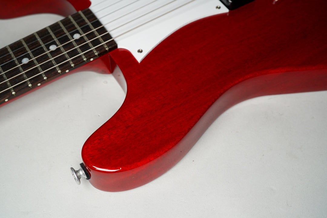 Close-up of the cherry red body's lower bout and cutaway, showing the strap button and part of the fretboard with dot inlays.