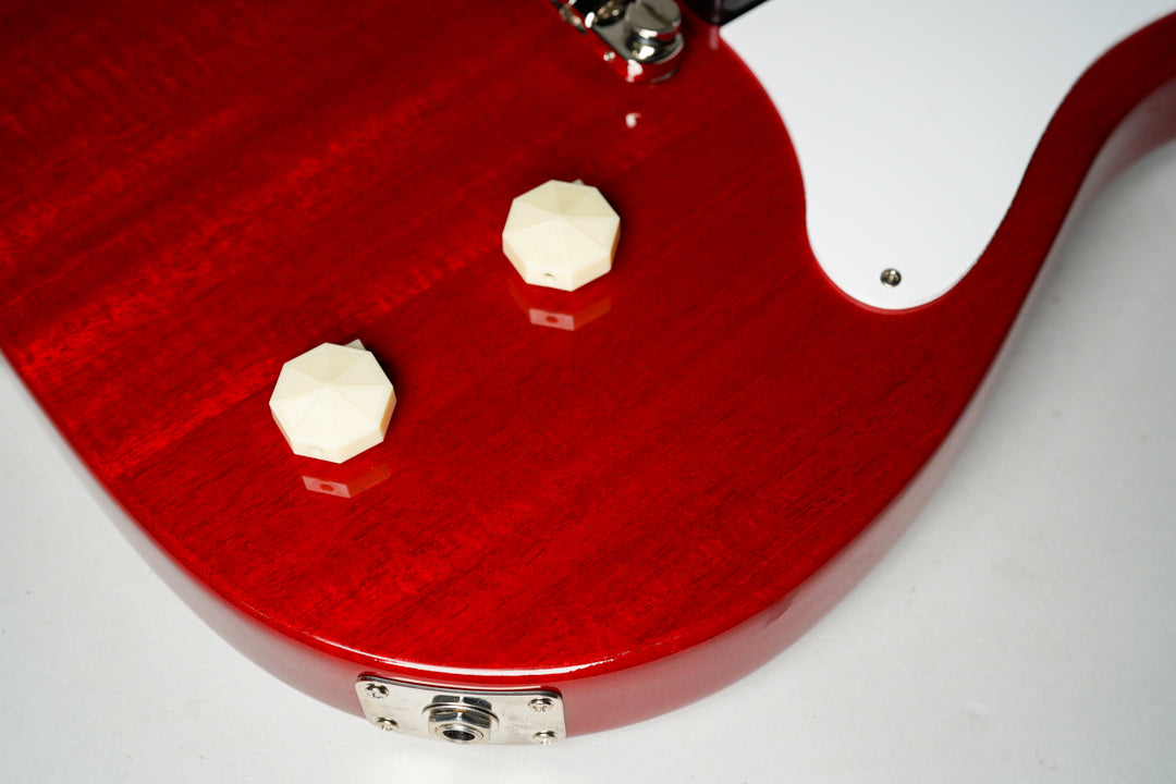 Close-up of the cherry red body, showing two cream octagonal control knobs, a white pickguard edge, and the chrome output jack.