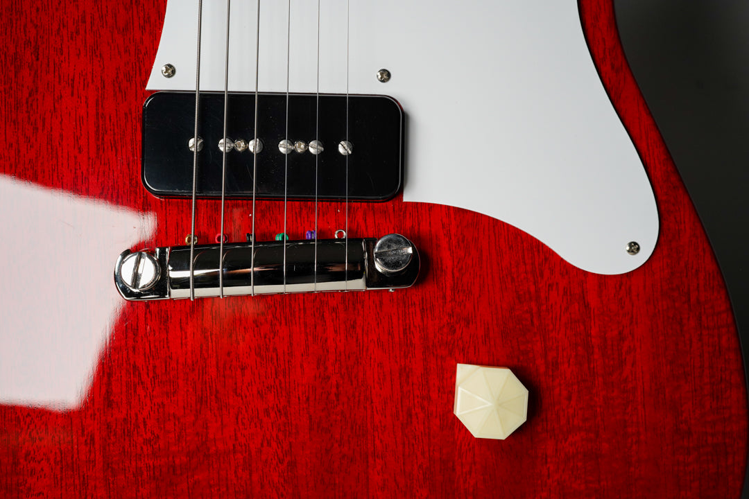 Close-up of the cherry red body, showing a black P90 pickup, chrome wraparound bridge, white pickguard, and an octagonal cream knob.