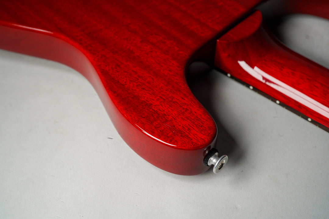 Close-up of the cherry red guitar body's lower bout and neck heel, showing the wood grain and a chrome strap button.