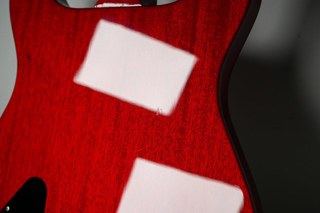 Close-up of the cherry red guitar's back, showing wood grain, a small ding, and reflections on the upper and lower body curves.