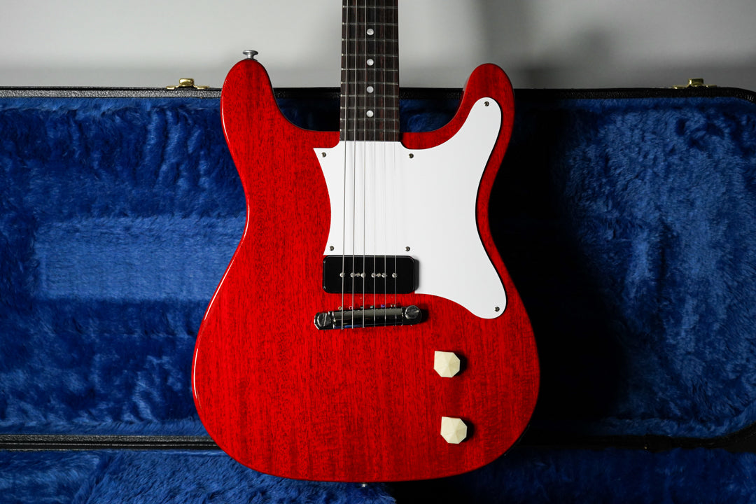 Cherry red electric guitar with a white pickguard, single P90 pickup, and two cream-colored control knobs, resting in a blue plush case.