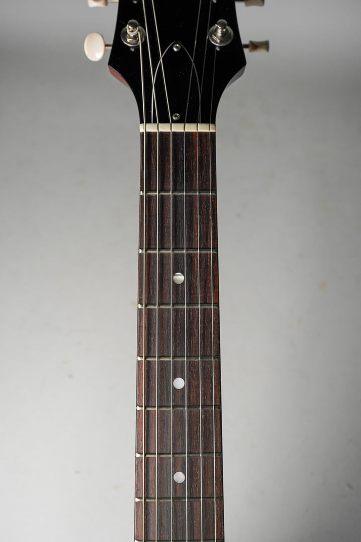 The dark rosewood fretboard with white dot inlays and a cream nut is framed from the headstock to the 7th fret.