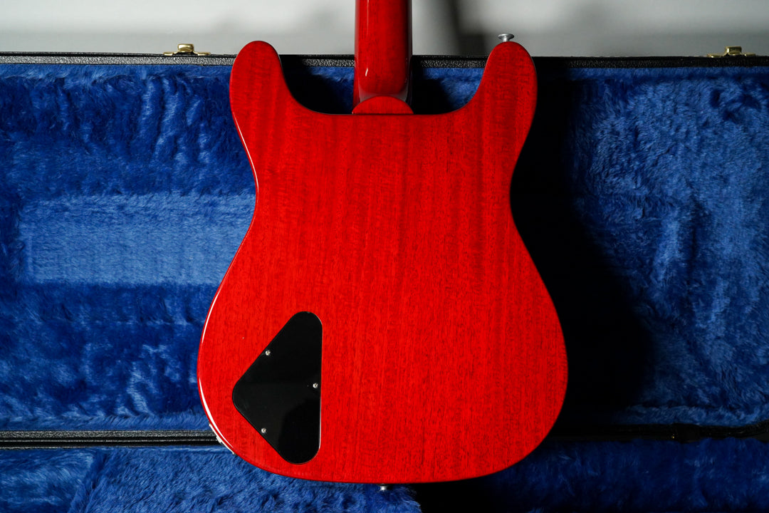 The back of a cherry red electric guitar with a visible wood grain and a black triangular control cavity cover.