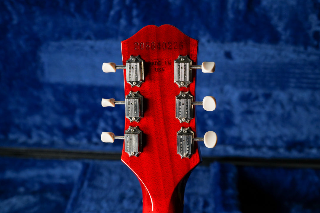 The back of a cherry red headstock with six cream-buttoned tuners, showing a serial number and "MADE IN USA" stamped into the wood.