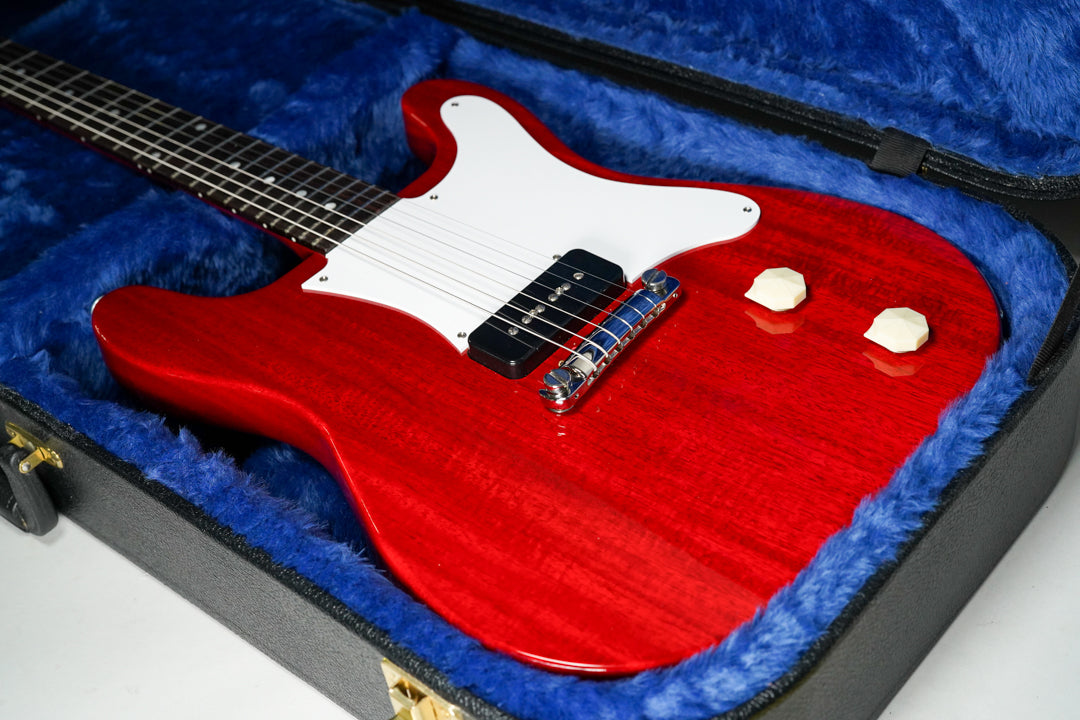 Cherry red guitar with visible wood grain, white pickguard, single black P90 pickup, and two cream-colored control knobs, resting in a blue-lined case.