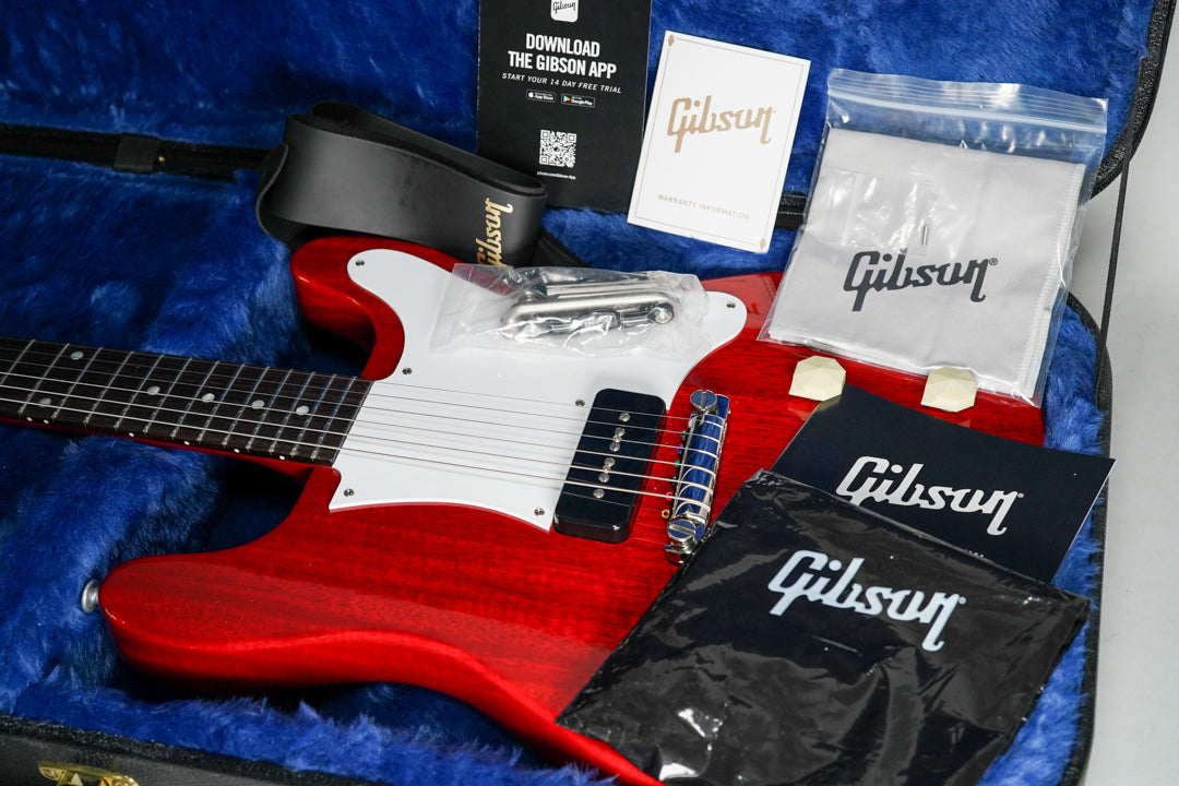 Cherry red guitar with a white pickguard and black P90 pickup, shown in a blue-lined case with accessories like a strap and cleaning cloth.