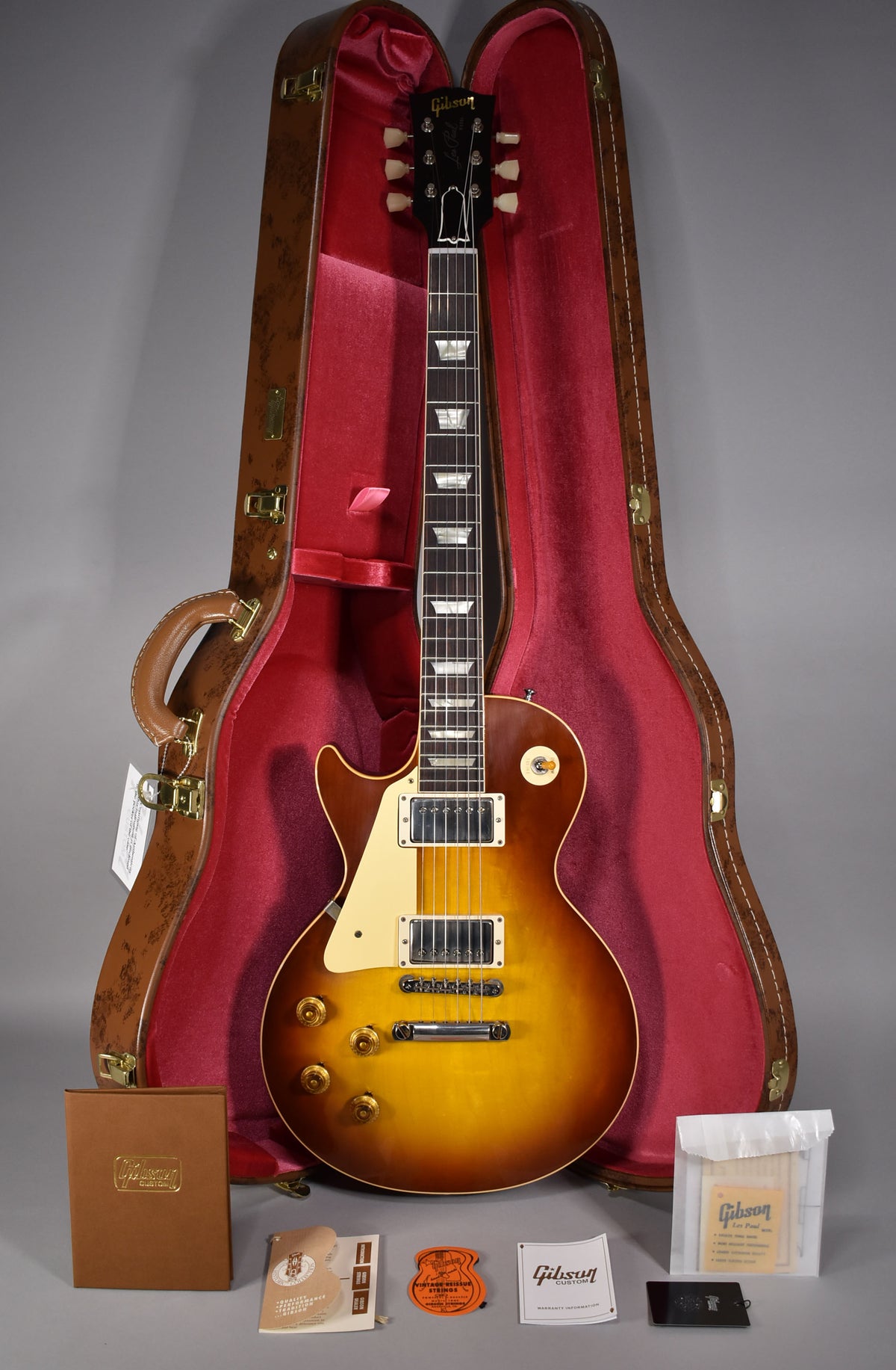Full-length view of a left-handed Les Paul in a brown-to-yellow sunburst finish, with a cream pickguard, in its open hard case.