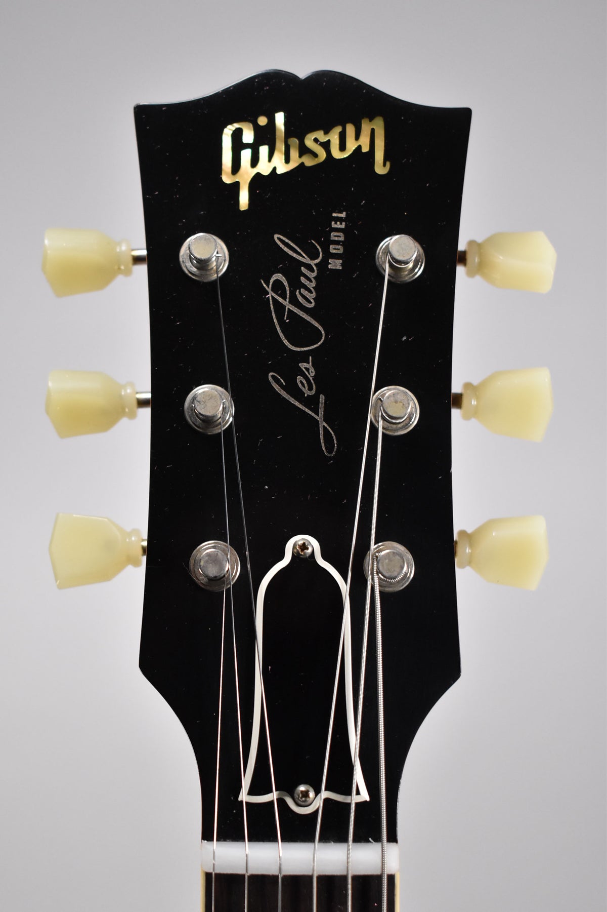 Close-up of the black headstock with cream tuning pegs, showing light wear and a bell-shaped truss rod cover.