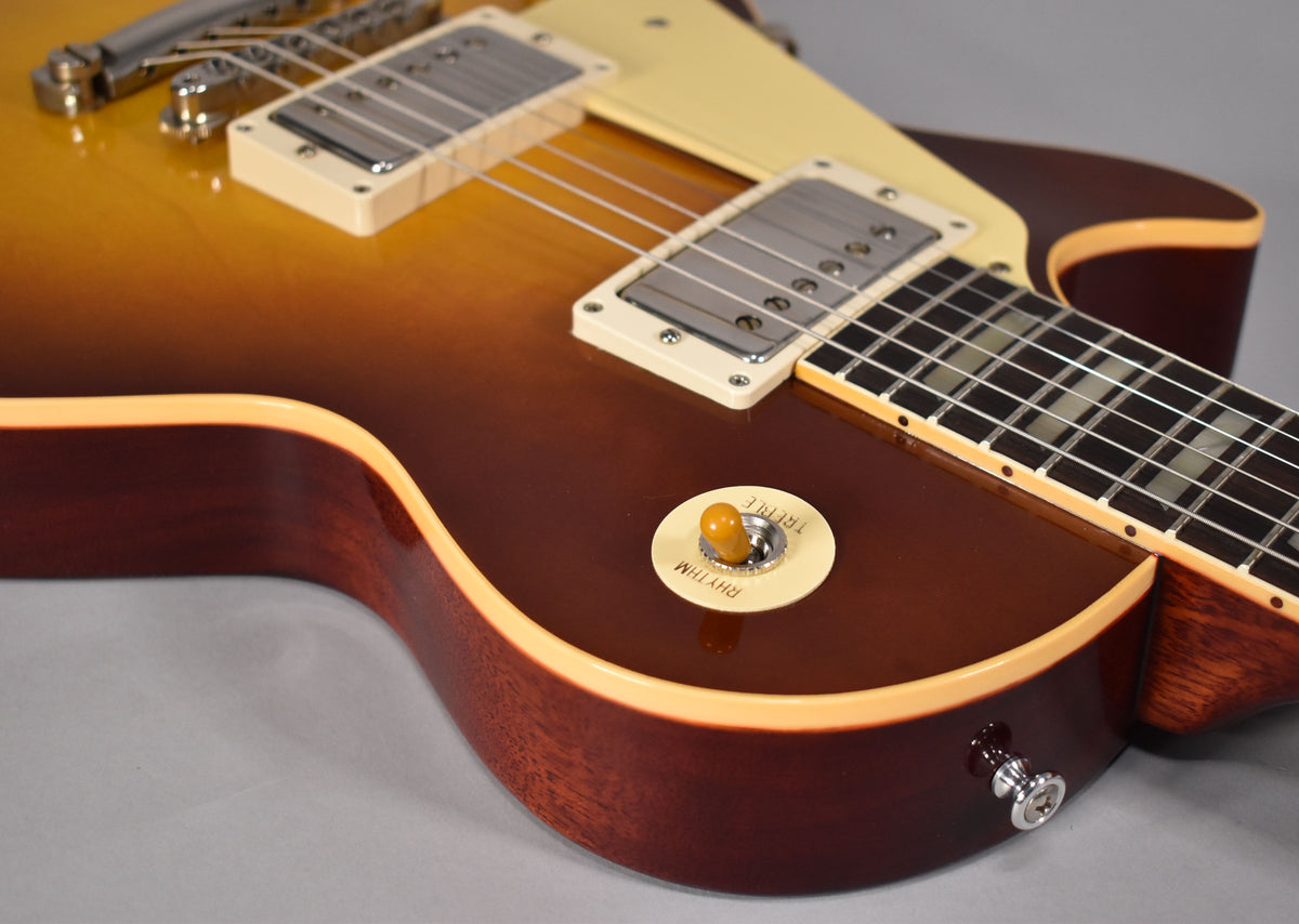 The guitar's lower body, showing the iced tea burst finish, cream binding, pickup selector switch, and output jack.
