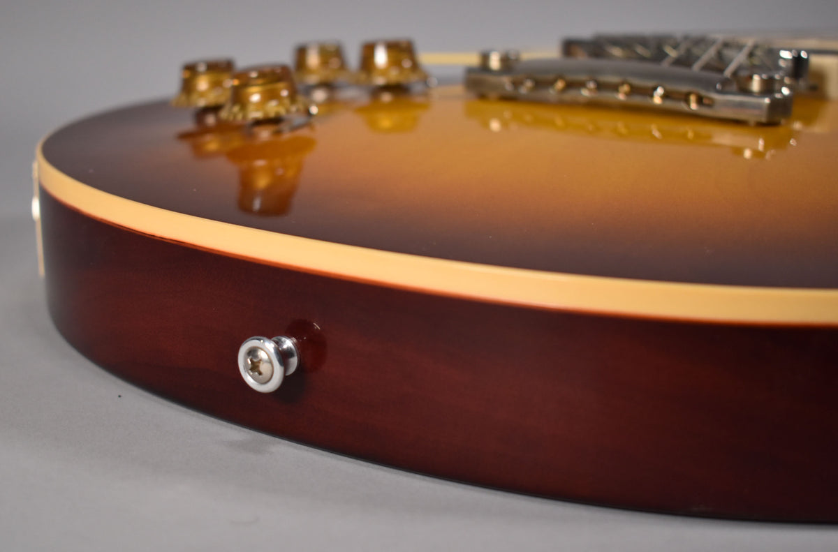 Close-up of the guitar's lower bout, showing the iced tea burst finish, cream binding, and a chrome strap button on the dark brown side.