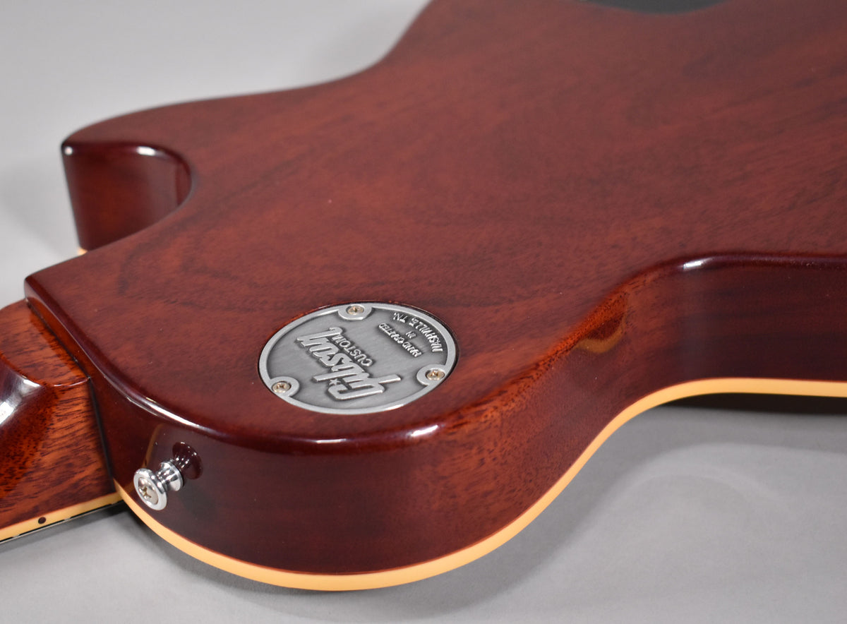 The back of the guitar's body, showing the dark brown finish, a metal medallion, and the strap button near the neck heel.