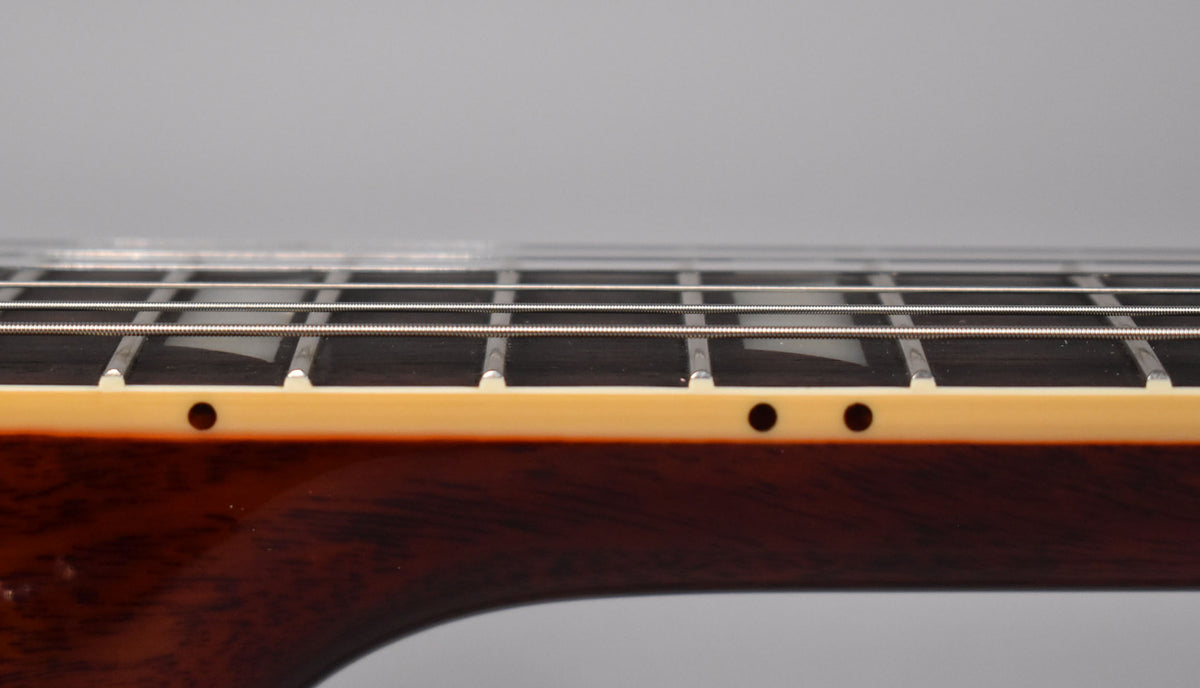 Close-up of the guitar's dark brown neck and cream binding, showing the frets, strings, and three black side dot markers.