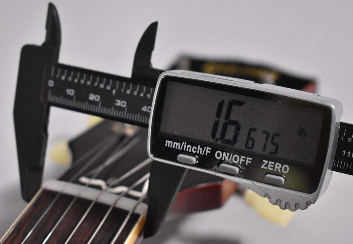 A digital caliper measures the nut width of the dark rosewood fretboard, displaying "1.6675 in" on its screen.