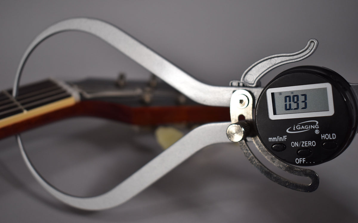 A digital caliper measures the guitar's neck thickness at the first fret, displaying 0.93 inches.