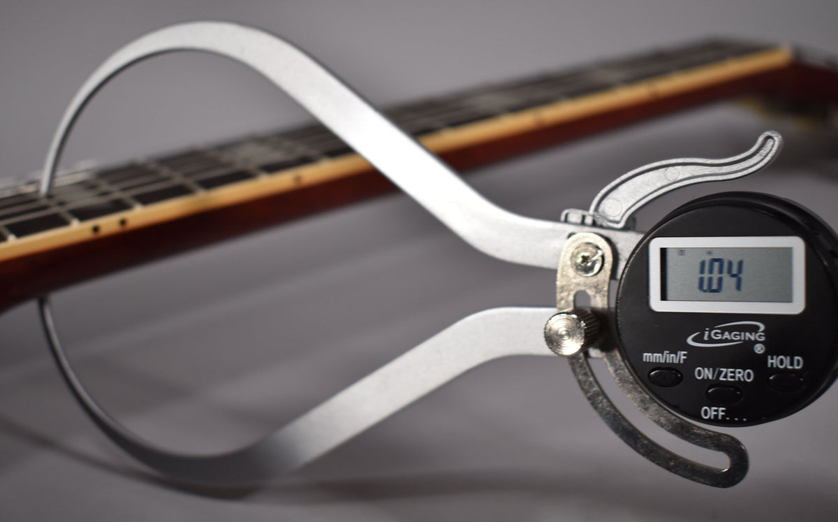 A digital caliper measures the fret height on the guitar's dark rosewood fretboard, displaying "1.04" on its screen.