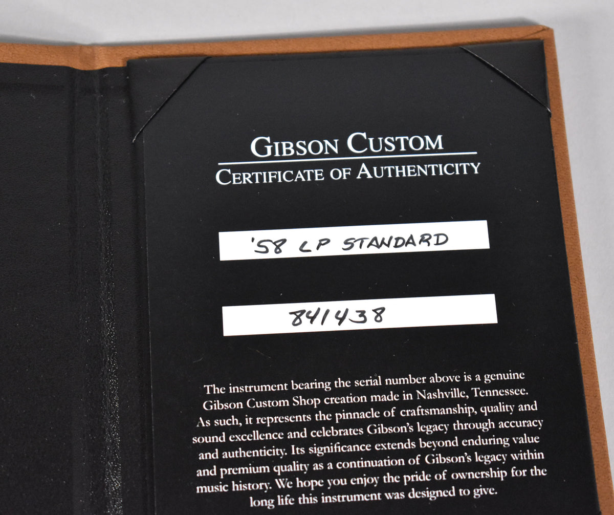 The guitar's Certificate of Authenticity, a black card with white text, is held in a brown leather folder.