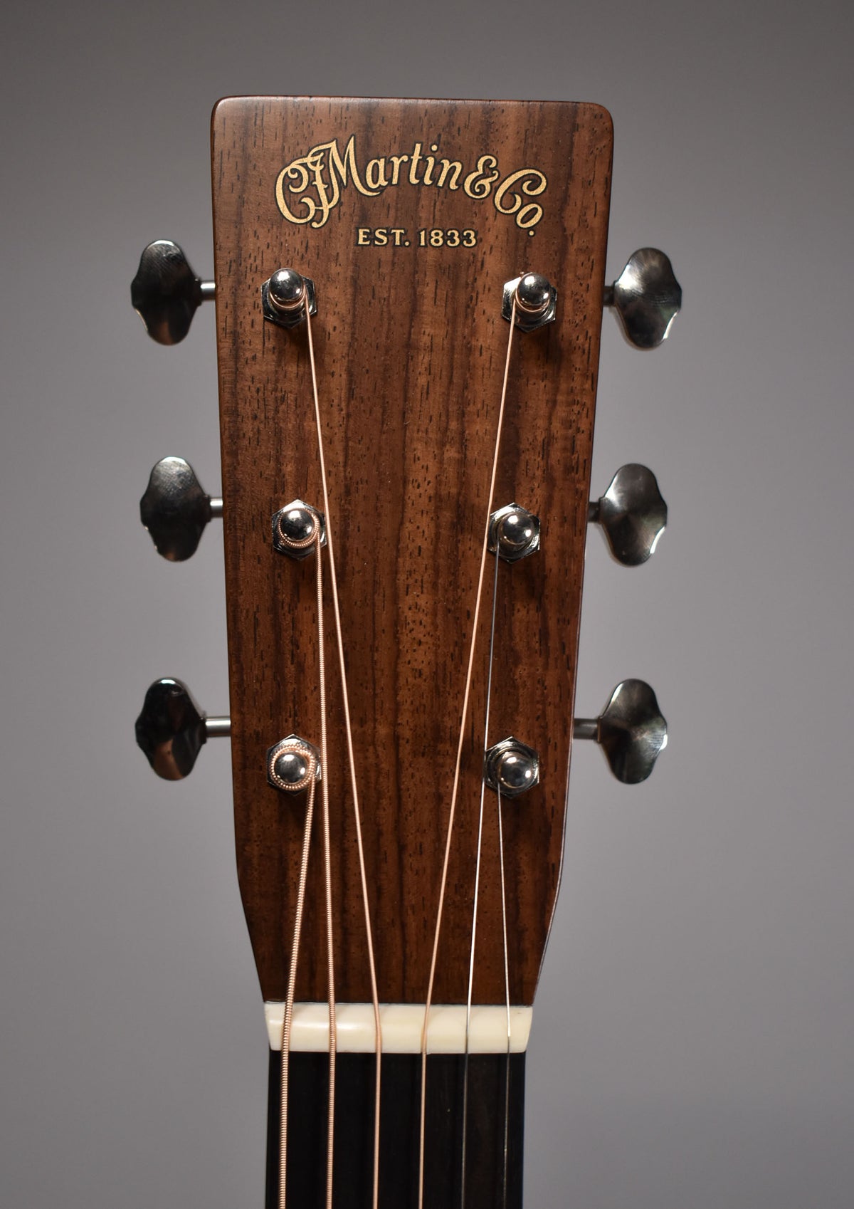 Close-up of the dark brown wooden headstock, showing six metal tuners with kidney-bean buttons and the top of the white nut.