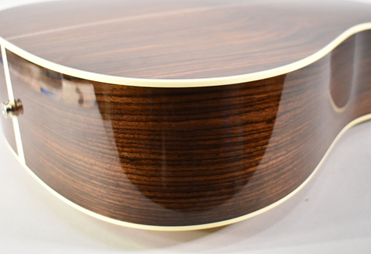 Close-up of the guitar's lower bout, showing the dark, highly figured wood grain of the glossy sides with cream binding.
