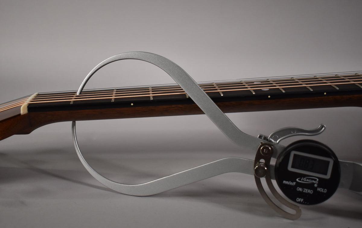 A digital fret height gauge measures the dark brown fretboard and frets of the guitar neck.