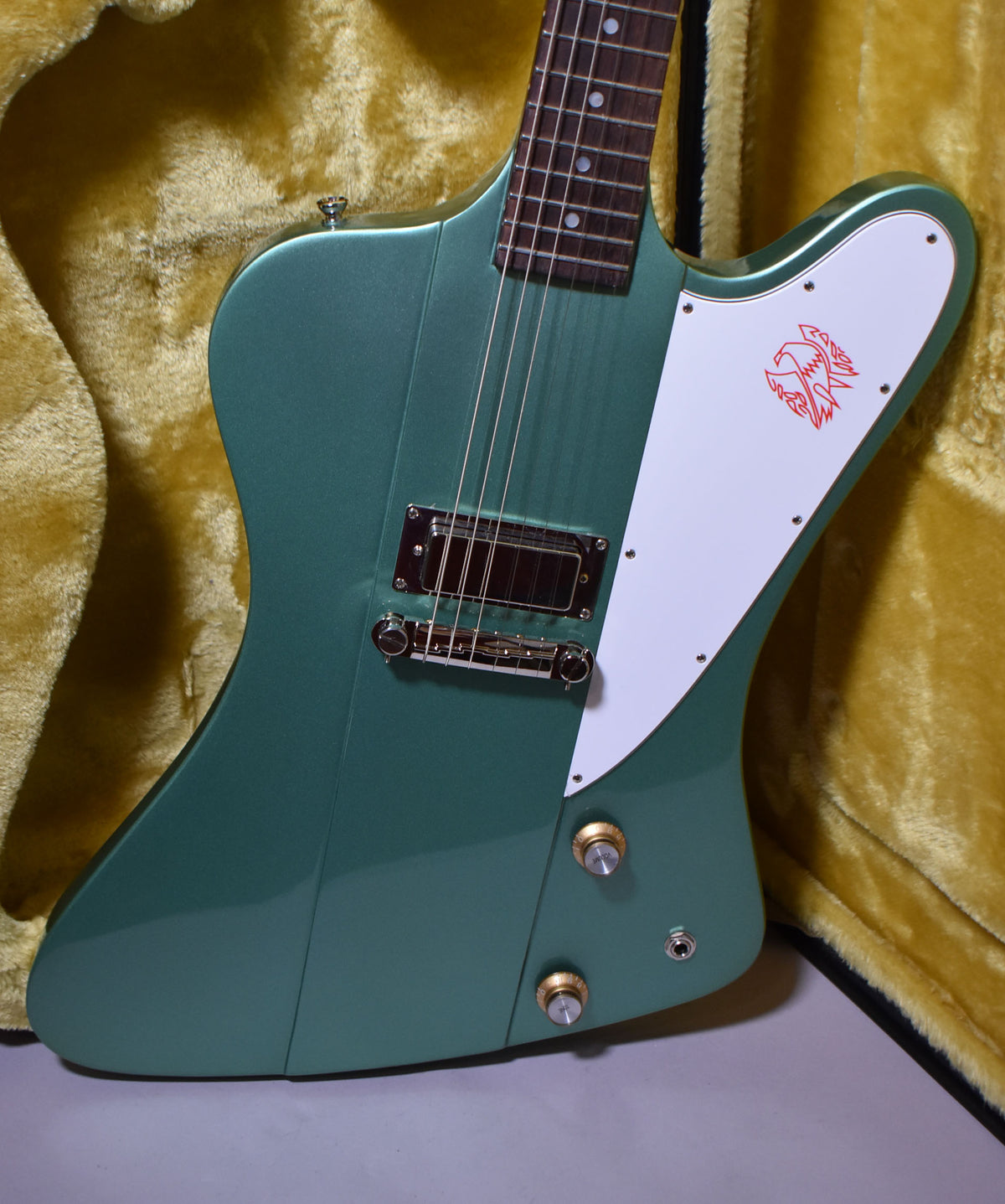 The Inverness Green Firebird's body and neck are angled, showing the white pickguard with a red bird graphic, a single humbucker, and two gold control knobs.