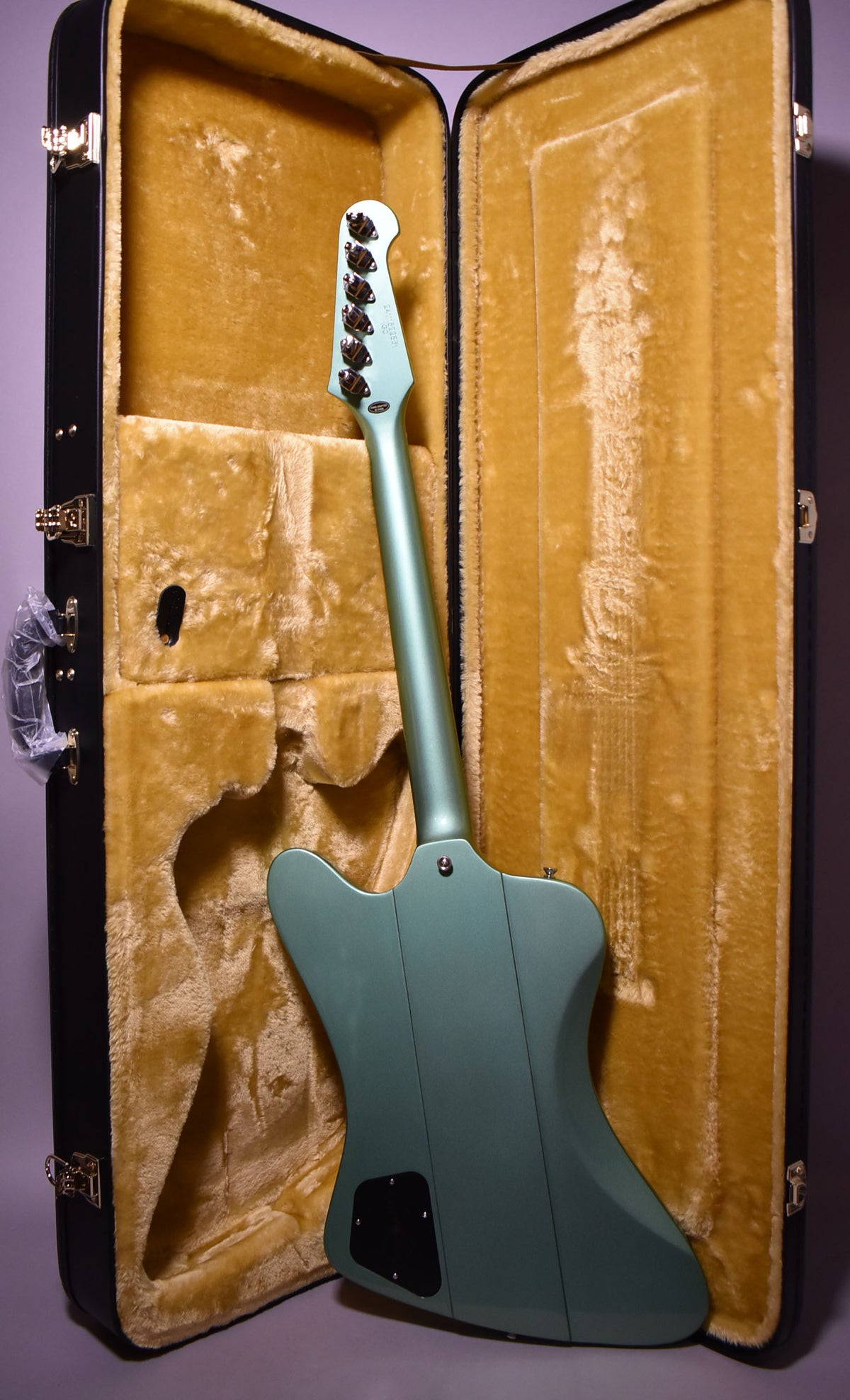 The back of an Inverness Green Firebird I guitar stands in front of its open, gold-lined hard case.