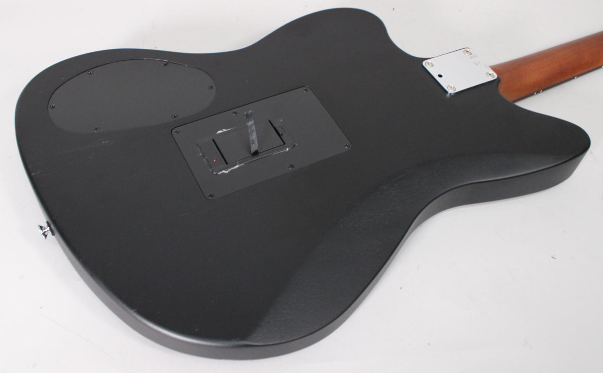 The black guitar's back is angled, showing a matte finish, two control plates, and a silver neck plate with a brown neck.