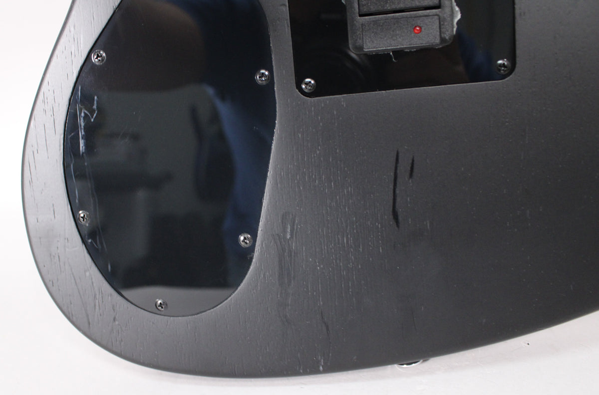 Close-up of the guitar's matte black body, showing a glossy black control plate with visible scratches and a red indicator light.