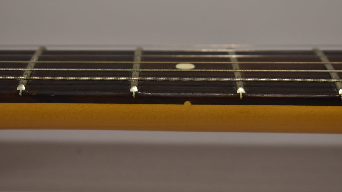 Close-up of the guitar's dark fretboard with light-colored frets and dot inlays, showing the side of the light-colored neck.