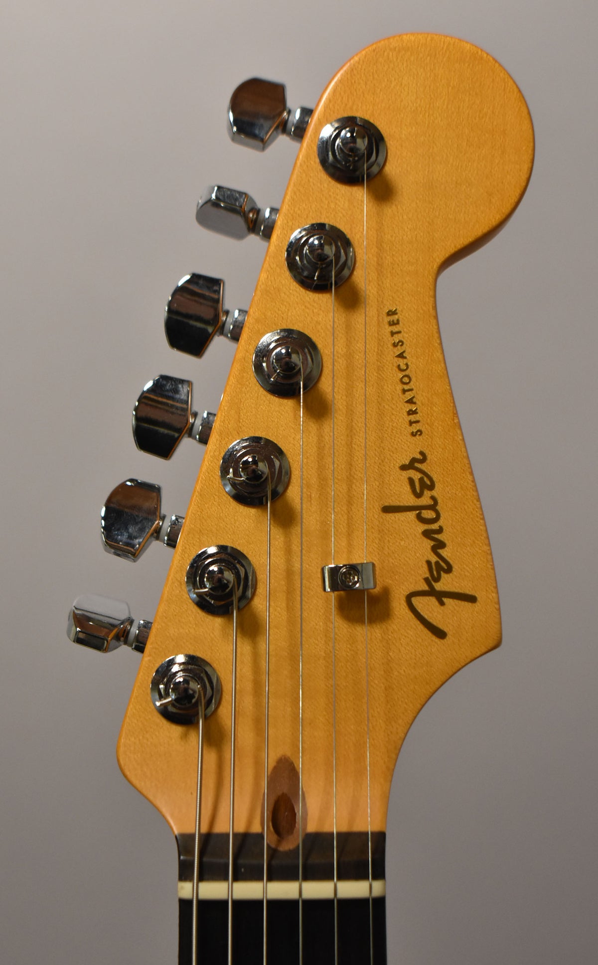 Close-up of the light brown headstock, angled slightly right, showing six chrome tuners, a string tree, and the truss rod access.