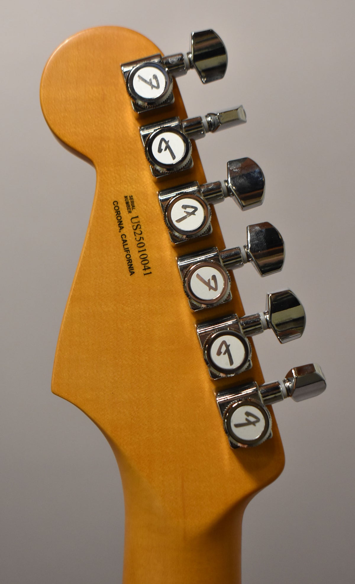 The guitar's headstock and top of the neck, viewed from behind, show six chrome tuning machines on a light wood finish.
