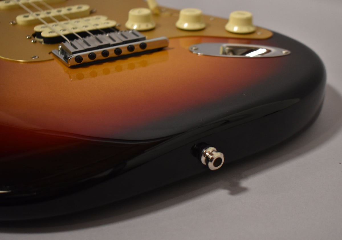 Close-up of the lower bout of a glossy Ultraburst Stratocaster, showing the gold pickguard, bridge, cream controls, and output jack.