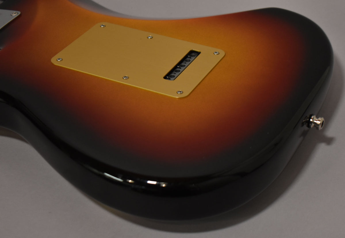 The guitar's lower body, in a glossy ultraburst finish, shows a gold tremolo cover with six string holes and a chrome output jack.