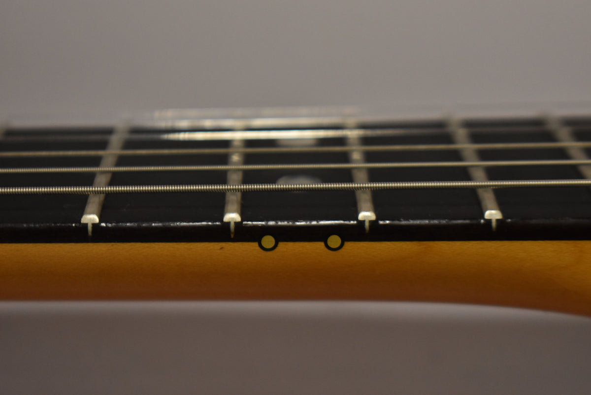 Close-up of the guitar's dark fretboard and light maple neck, showing two circular fret markers on the side.