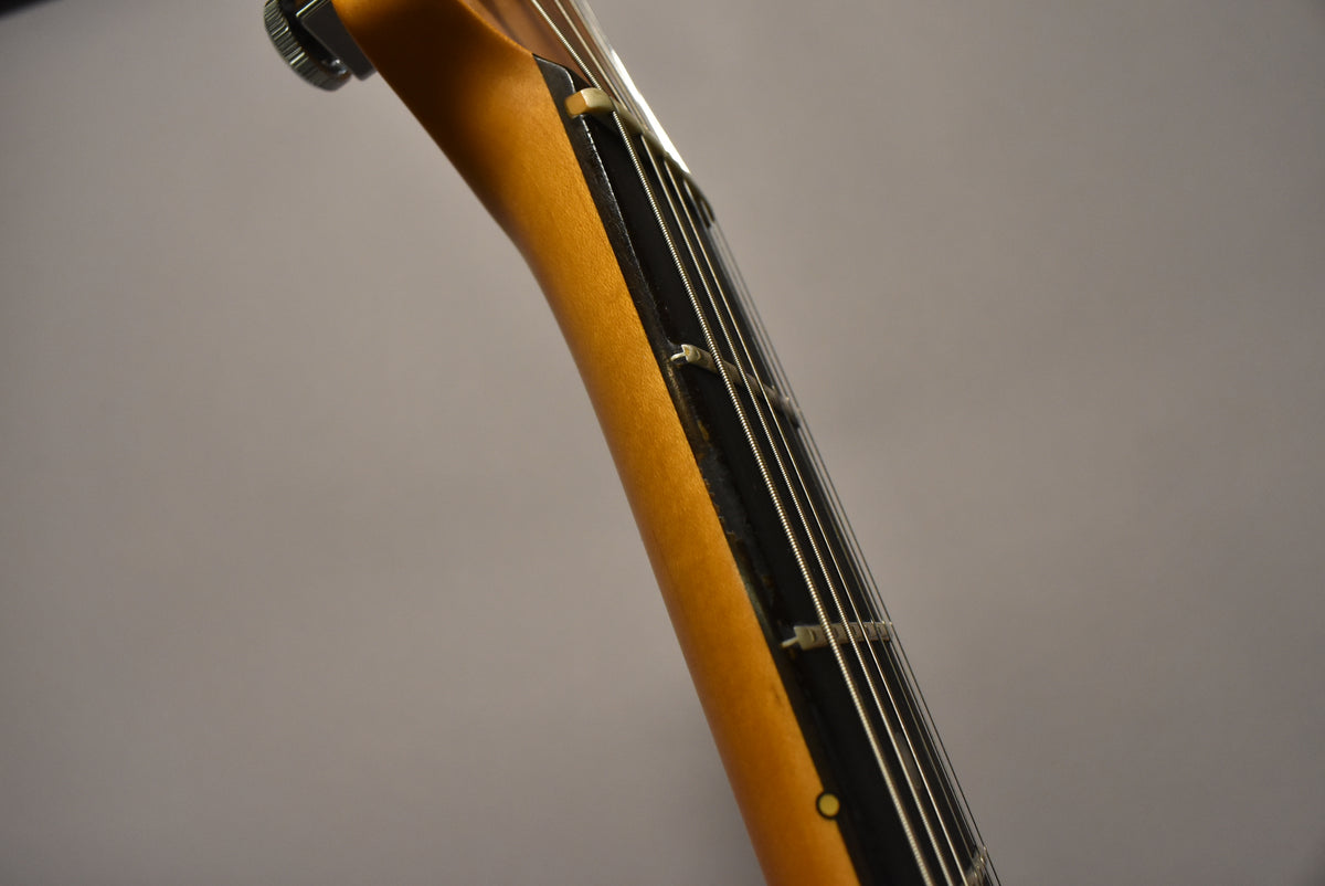 Close-up of the guitar neck, showing the light-colored wood and dark fretboard with white strings and a visible fret marker.