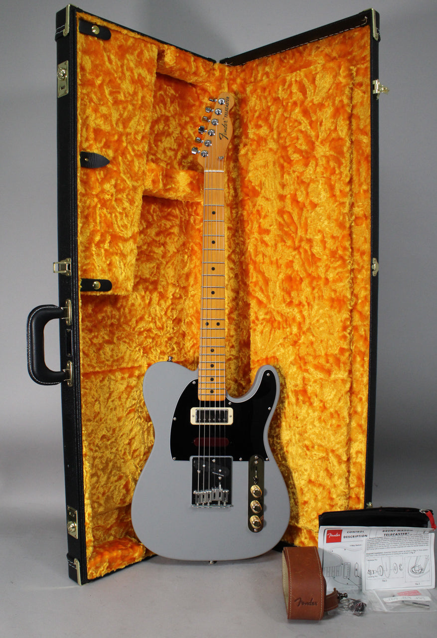 Full-length view of a matte primer gray Telecaster with a black pickguard, gold control plate, and a humbucker in the neck position, resting in its open, orange-lined hard case.