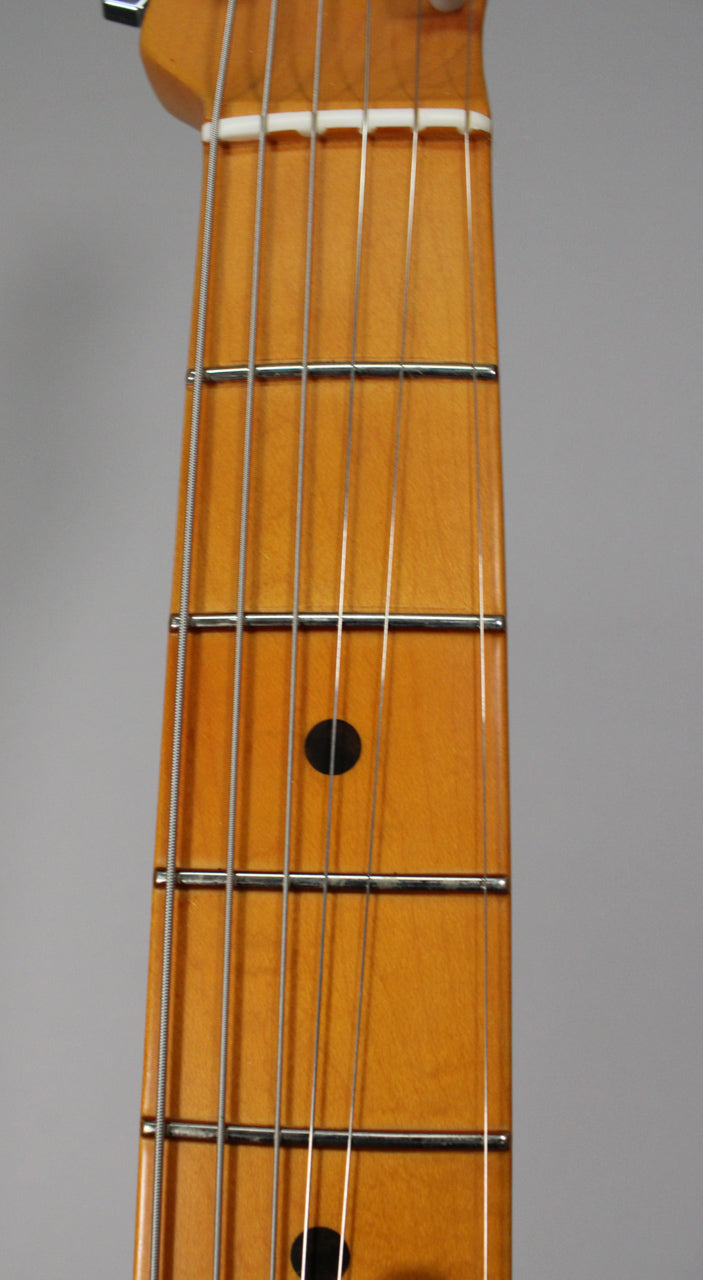 Close-up of the guitar's maple fretboard, showing the white nut, first five frets, and black dot inlays on the 3rd and 5th frets.