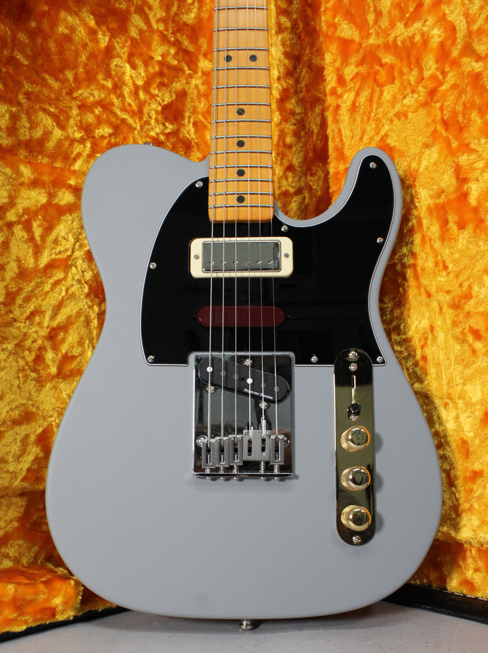 Full-body shot of a matte primer gray Telecaster with a black pickguard, gold control plate, and a maple fretboard.